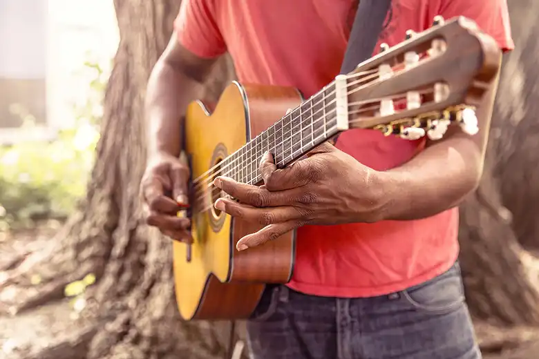 Hombre tocando guitarra acústica junto a un árbol