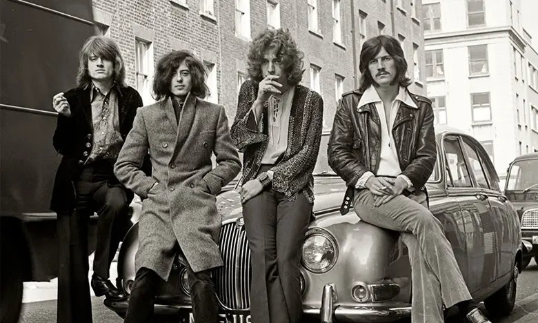 La imagen muestra a la banda británica Led Zeppelin sentados sobre la cajuela de un auto