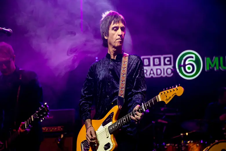 La imagen muestra a Johnny Marr tocando una guitarra Jaguar en el escenario