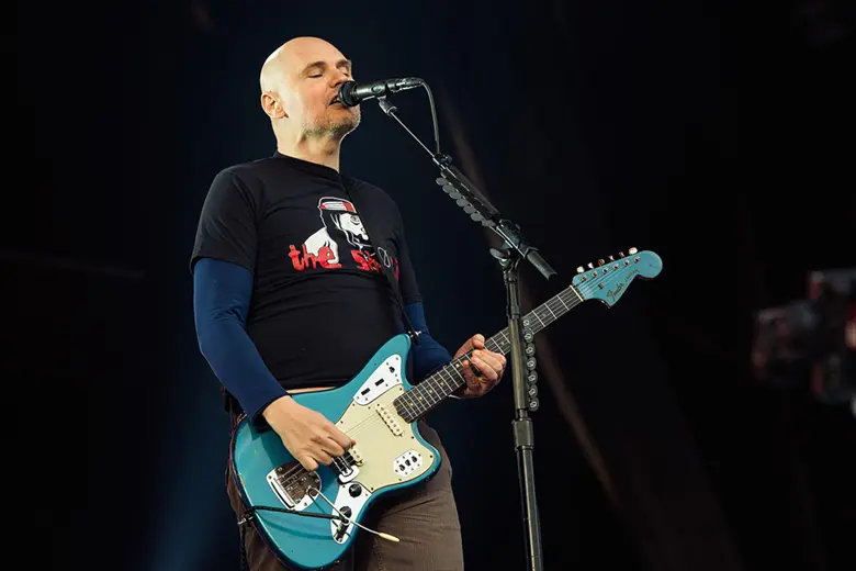 La imagen muestra a Billy Corgan de los Smashing Pumpkins tocando una guitarra Jaguar en el escenario