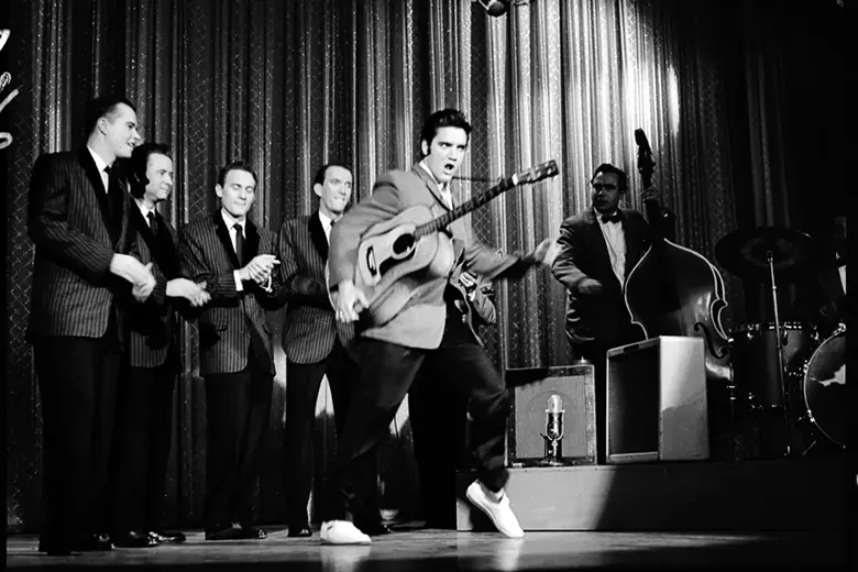 Es una imagen en blanco y negro de Elvis Presley tocando en vivo en los años 50