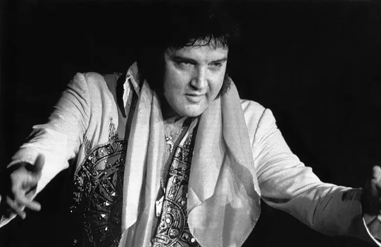 Es una imagen en blanco y negro que muestra a un Elvis Presley con sobrepeso en el escenario