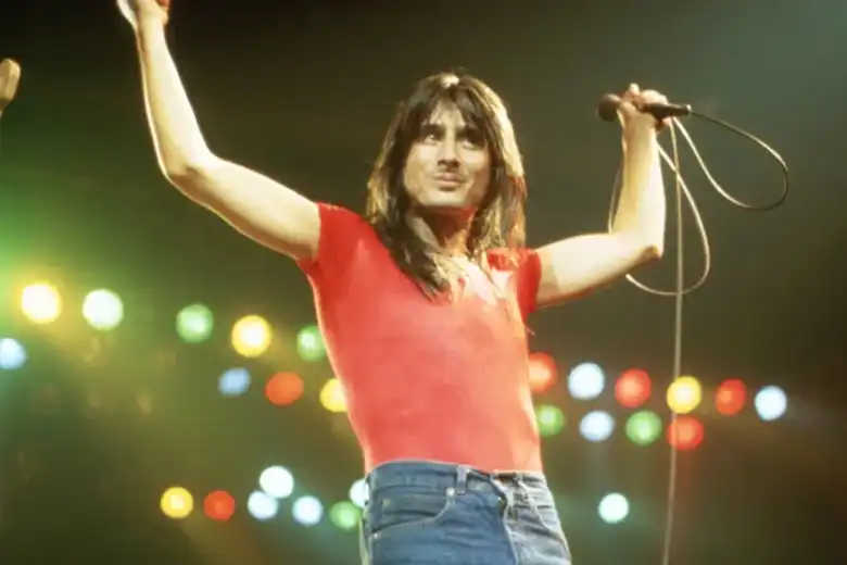 La imagen muestra al cantante de Journey, Steve Perry, sobre el escenario con sus brazos alzados