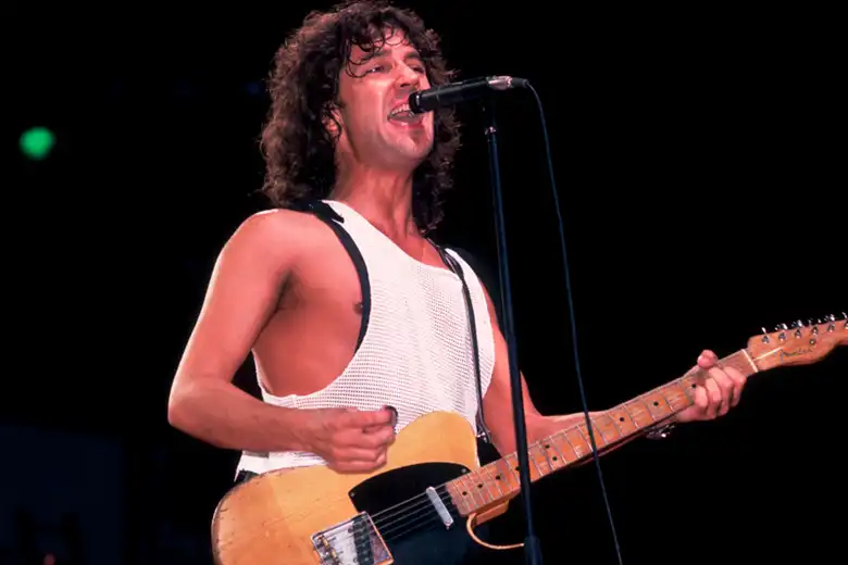 La imagen muestra a Billy Squier actuando en vivo sobre el escenario