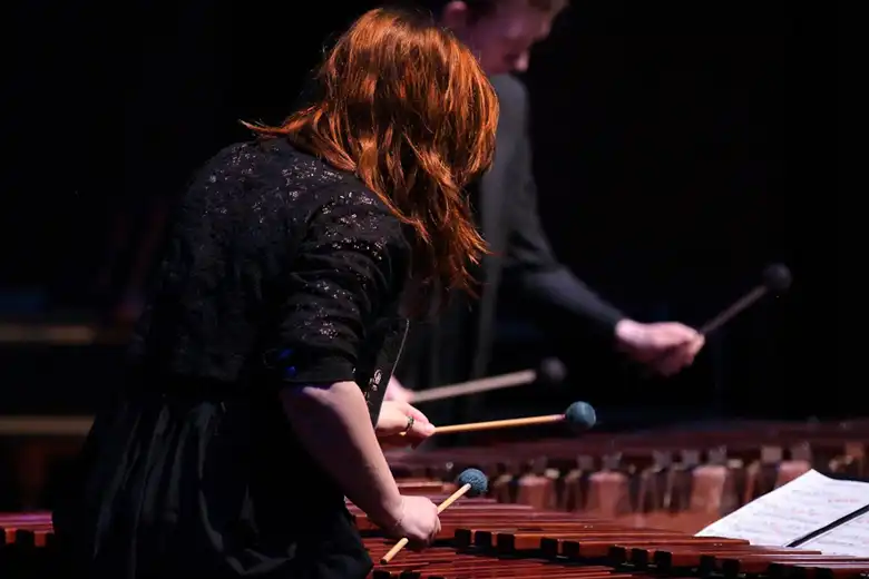 La imagen muestra a una mujer y a un hombre tocando marimbas sobre un escenario.