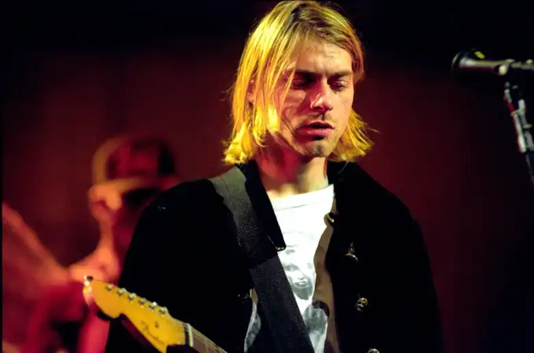 La imagen muestra a Kurt Cobain de Nirvana tocando su guitarra sobre el escenario.