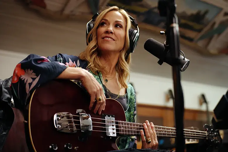 La imagen muestra a Sheryl Crow en un estudio de grabación con una guitarra.